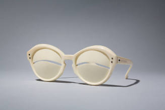 Ivory sunglasses with curved slit at eye center; gold metal studs at temples; stamped Depose an…
