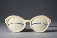 Ivory sunglasses with curved slit at eye center; gold metal studs at temples
