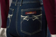 Detail view of dark blue denim jeans showing back pockets with yellow topstitching, embroidered…