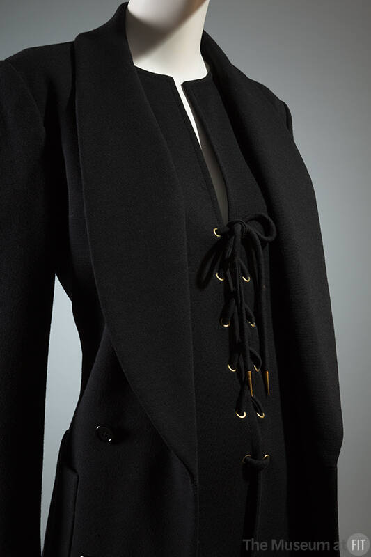 Black shawl collar jacket over black deep V-neck top with lace up front closure and gold gromme…