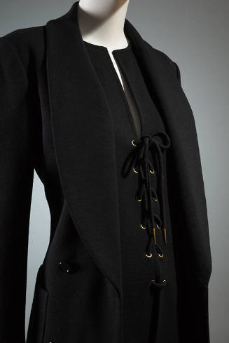 Black shawl collar jacket over black deep V-neck top with lace up front closure and gold gromme…