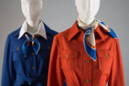 Detail view of cobalt blue uniform jacket with blue, white and orange neck scarf next to orange…