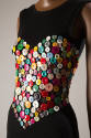 Detail view of black sleeveless dress showing heart shaped bustier design made of various butto…