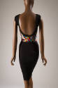 Back view of black sleeveless dress showing plunging back and button embellishment extending ac…