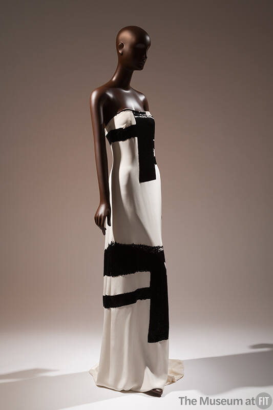 ¾ view of white strapless floor length evening dress with thick black brushwork motifs througho…