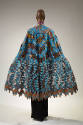 Back view of cape ensemble showing blue and brown cotton and lace cape with floral motifs and f…
