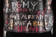 Detail view of back bottom hem of black leather jacket showing graffiti writing “Pygmy” and “We…
