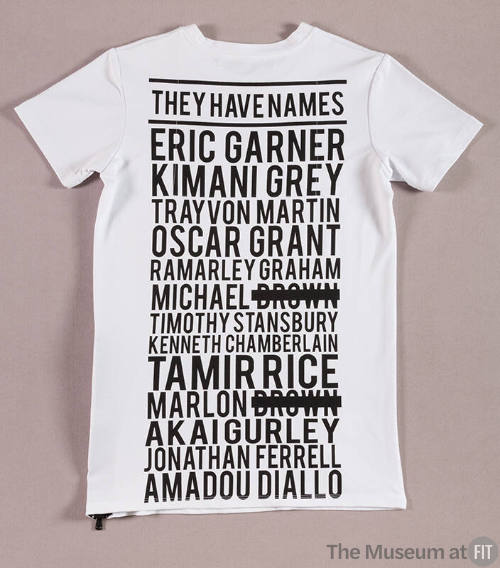 White short sleeve t-shirt covered in black writing reading “They have names” and 13 names with…