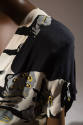 Shoulder detail of dress printed with gray stones with black shadows and yellow symbols, short …
