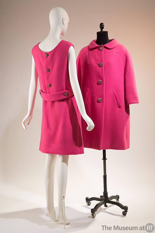 Pink skirt suit shown from the back: sleeveless blouse features three large buttons and a marti…
