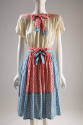 Knee-length dress with off-white blouson bodice and blue gingham skirt and tie with red gingham…