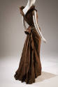 Back view of brown/green evening dress showing V-back, fabric gathered into small bustle and sl…
