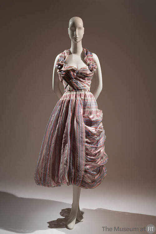 long, strapless, asymmetrical dress with pink metallic, light purple, grey, and white stripes; …