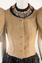Detail of beige grasscloth button front jacket, bead and cowrie shell neckpiece, black rafia sk…