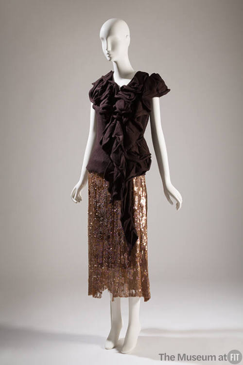 Evening ensemble of dark brown sleeveless top with asymmetrical front ruffle and calf length br…