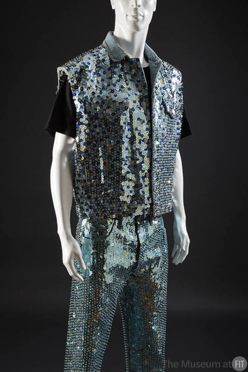 Light blue denim ensemble: sleeveless jacket and jeans covered with large varying blue, silver,…