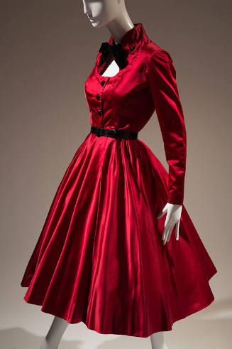 Red long sleeve cocktail dress with pleated calf length skirt and narrow, black belt at waist