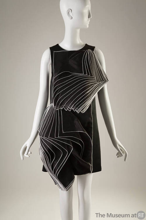 Black sleeveless short dress with stacked square layers outlined in white opening diagonally on…
