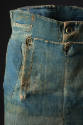 Detail view of blue denim trousers showing ivory buttons on drop front and along waistline, coi…