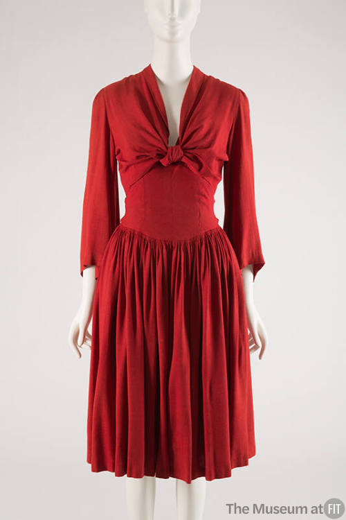 Red knee-length dress with pleated skirt and long bell sleeves and tie panels that knot at cent…