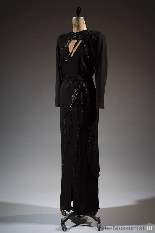 Floor-length black dress with triangular cut out at the bust and black sequin elements
