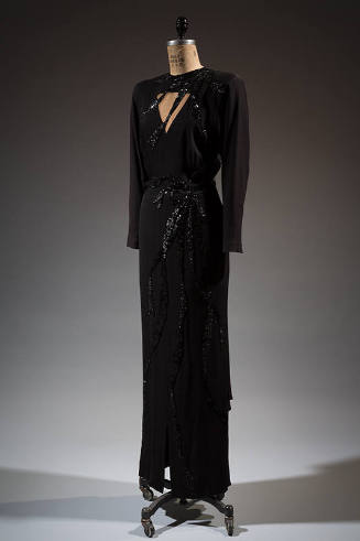 Floor-length black dress with triangular cut out at the bust and black sequin elements

