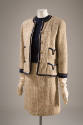 Beige three-piece suit of collarles jacket with navy blue trim and gold metal buttons with shor…