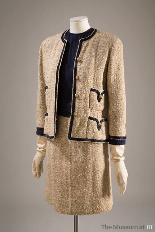 Beige three-piece suit of collarles jacket with navy blue trim and gold metal buttons with shor…