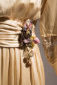 Detail view of cream dress showing waist sash tie with blue, pink and gold metallic flower orna…