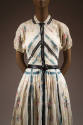 Detail of white short sleeve dress with floral print, blue and black trim and pleated skirt
