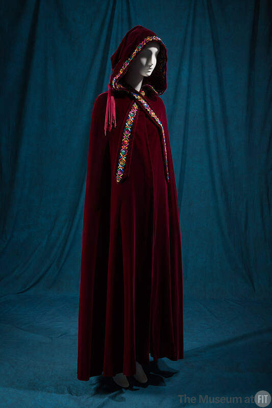 Red floor length hooded cape with multicolor embroidered trim, tassel hanging from hood