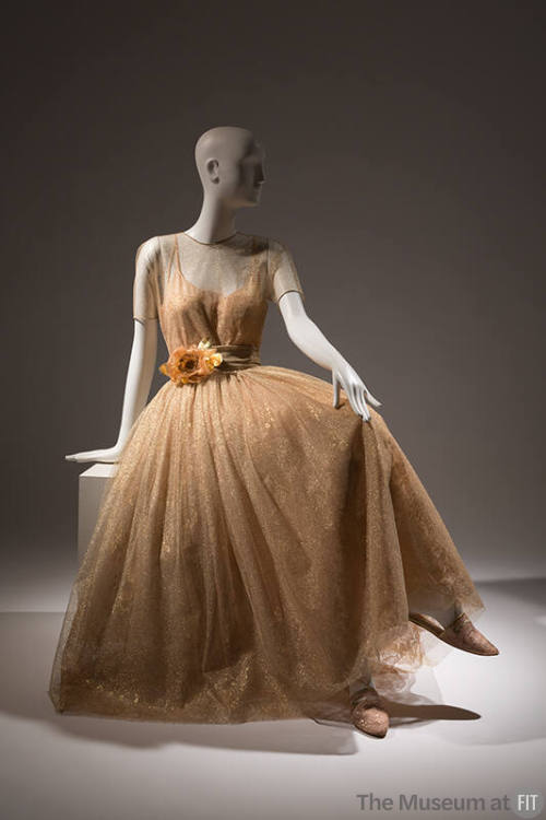 Sheer gold dress with short sleeve bodice over slip with full skirt, large flower at waist cumm…