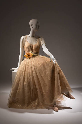 Sheer gold dress with short sleeve bodice over slip with full skirt, large flower at waist cumm…