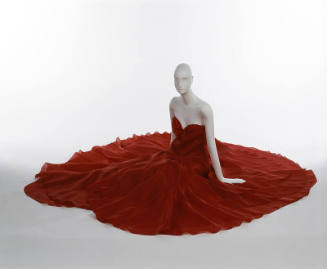 Seated mannequin in red strapless dress with petal-like layers, full skirt spread out