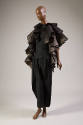 Black metallic pleated cape in ruffled tiers over black tiered peplum top and matching tapered …