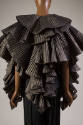 Back of black pleated cape showing pleated metallic fabric with circular tiers of ruffles