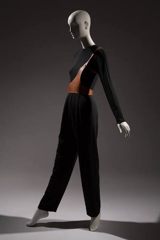 Black long sleeve jumpsuit with one strap brown leather harness over right shoulder and around …