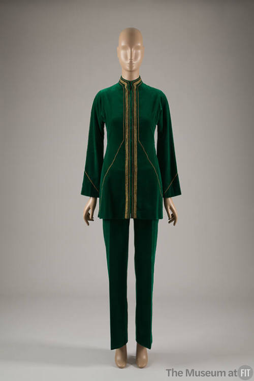 Green pantsuit of tunic jacket with stand collar and gold metallic ribbon and braid edging and …