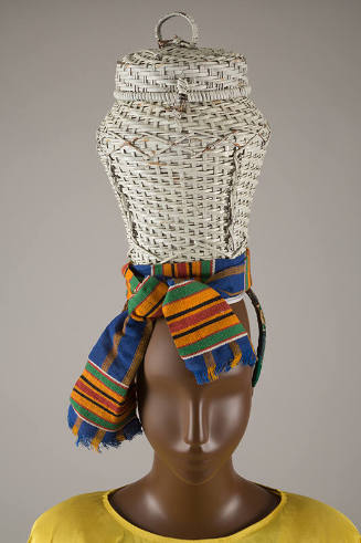 Detail view of wicker basket hat showing green, orange, black, red and white Kente cloth sash t…