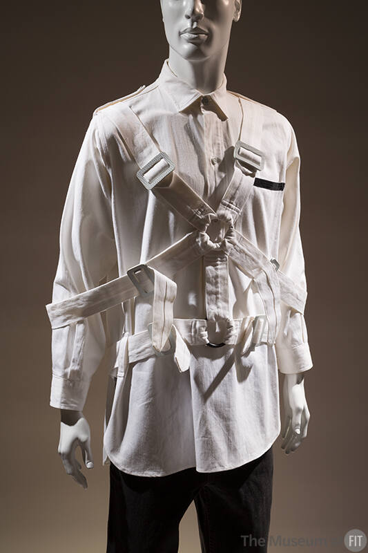 Man’s white oxford style shirt with multiple buckled straps overtop and linked with two front r…