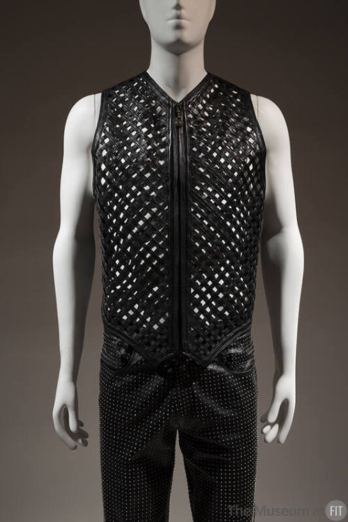 Black zippered vest with lattice front strips, belt buckle embossed with classical motifs style…