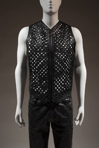 Black zippered vest with lattice front strips, belt buckle embossed with classical motifs style…