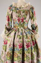 Back view of mauve floral brocade gown showing fitted bodice and full knife pleat skirt flaring…
