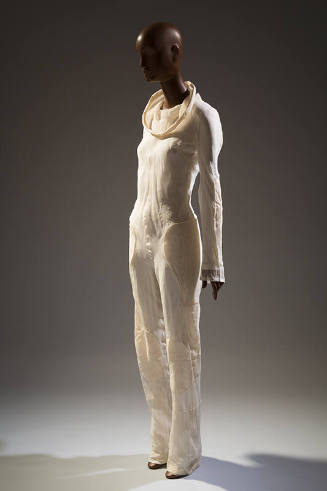 Ivory jumpsuit with funnel cowl neckline, long sleeves and padded patches at hip, thigh and kne…
