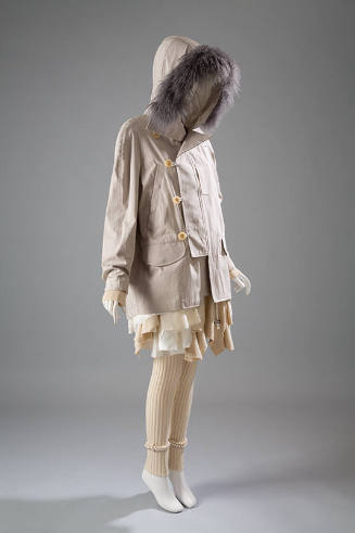 Beige coat with button and loop closure and hood trimmed in grey fur over off-white dress with …
