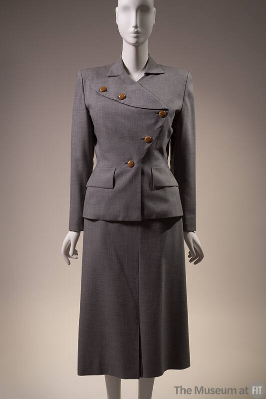 Grey suit with long sleeve jacket with asymmetric brown button front, flap pockets and matching…
