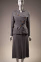 Grey suit with long sleeve jacket with asymmetric brown button front, flap pockets and matching…