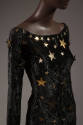 Detail of black crushed velvet long sleeve dress with gold metal stars at neckline and scattere…