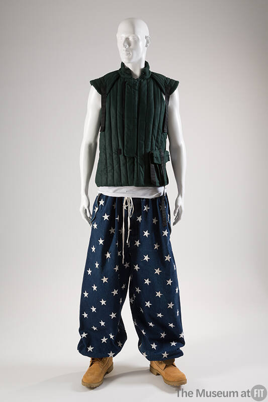 Dark teal green padded vest with vertical quilting; loose, navy pants with white star pattern; …