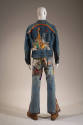 Back view of man’s blue denim jacket embroidered with man, animals and rainbow and bell bottom …
